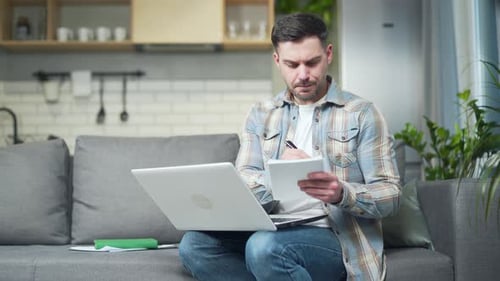 Man Uses Laptop and Notebook on Couch