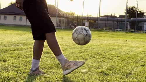 Young Man Juggling Soccer Ball on Stadium at Sunset Professional Footballer Kicking Ball at Green