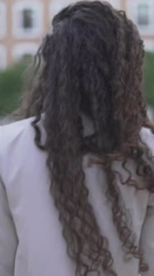 Moroccan Woman With Long And Curly Hair Walking On City Park At Daytime Back View