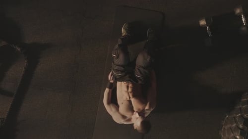 Shirtless Man Performing Ab Crunches in Dark Gym