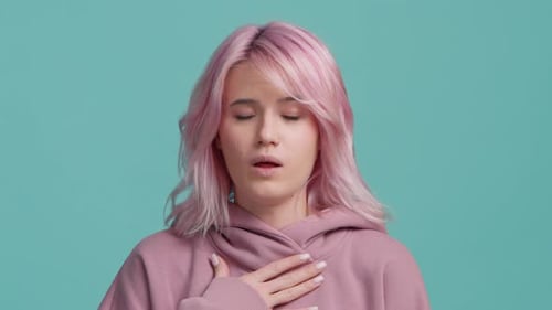 Joven estudiante poco saludable, cabello rosado, toca el cuello, tos intensa, garganta