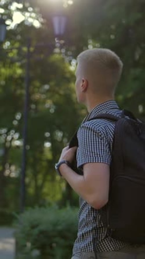 Vertical of Side View of a Student Photographer is Walking Along a European Town Street Behind Him
