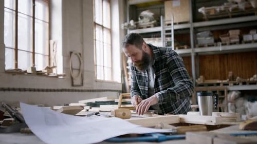 Carpenter sketching product design looks at camera in his workshop small business
