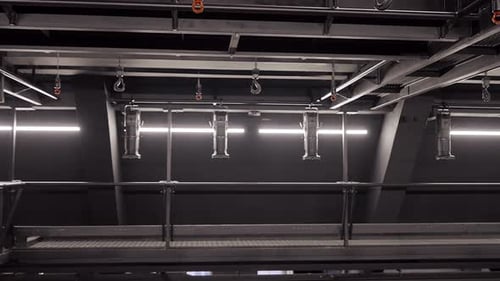 In a Black Industrial Room, Several Chain and Belt Hoists Lower Hooks and Loops.