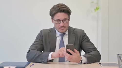 Middle Aged Businessman Browsing Internet on Smartphone in Office