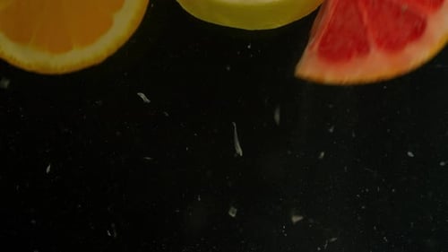 Los cítricos caen al agua sobre un fondo negro