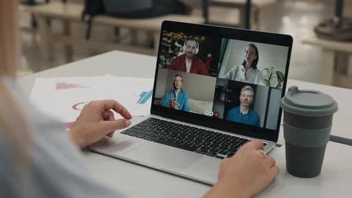 Woman Participates in Online Meeting with Colleagues Via Laptop in Modern Office Setting