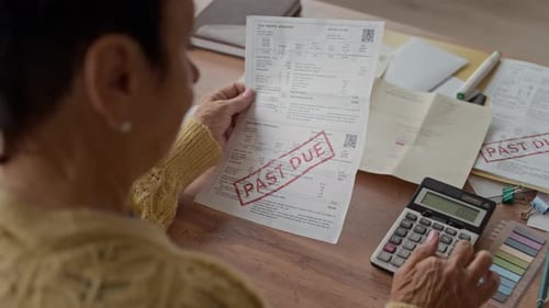 Senior Woman Checking Overdue Bill and Using Calculator at Desk