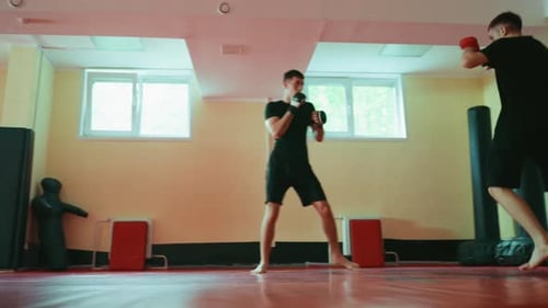 Zwei Kämpfer beim Sparring im Fitnessstudio auf roter Matte und tragen barfuß Handschuhe