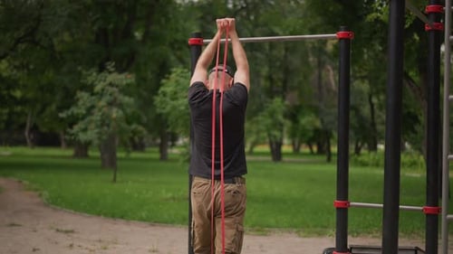 Person macht Widerstandsbandtraining auf einem ruhigen Parkweg, Person, die den Arm über dem Kopf ausführt