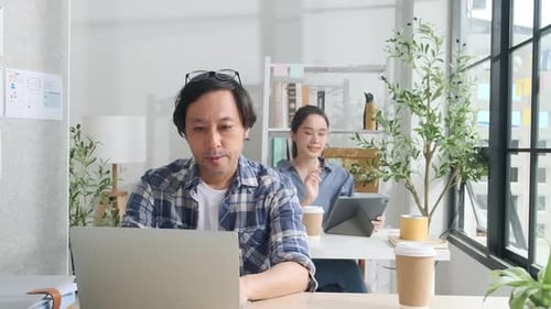 Two young Asian startup partners are working in a casual small business office.