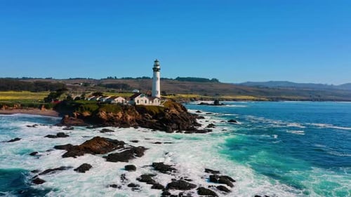 Flight towards a lighthouse on the California coast with waves crashing below.