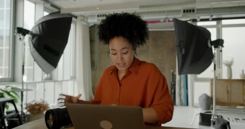 African American Female Photographer sitting in her Studio checking Camera and using Laptop