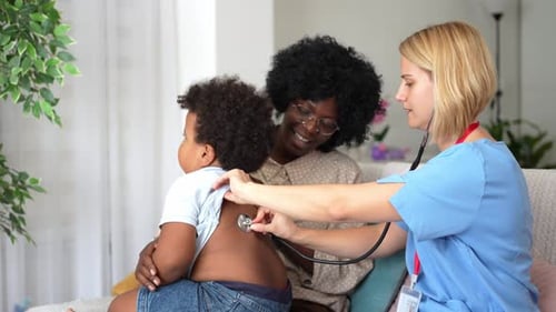 Female doctor visiting a family and performing a check-up on a toddler boy sitting in his mother's l