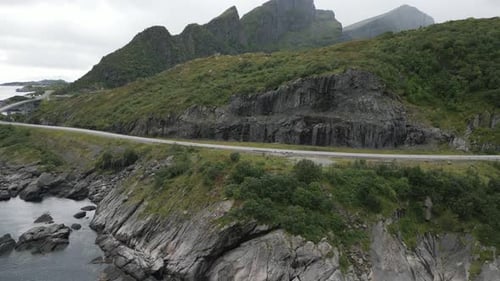 Aerial view showing a black vehicle moving along a road that winds along the mountains and the ocean