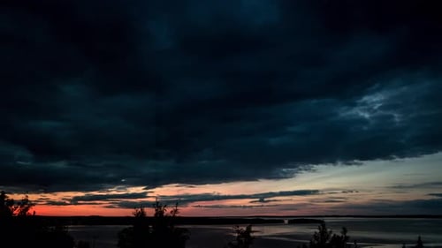 Dark clouds passing over a sunset. Calm lake and forest sway in the wind.