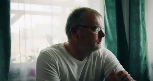 Man in Glasses Looks Out of Sunny Window