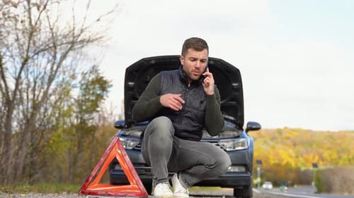 Road Side Warning Triangle Warning Oncoming Traffic of a Broken Down Car with a Man Using His Cell