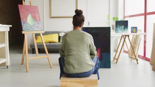 Video of back view of biracial female artist painting in studio