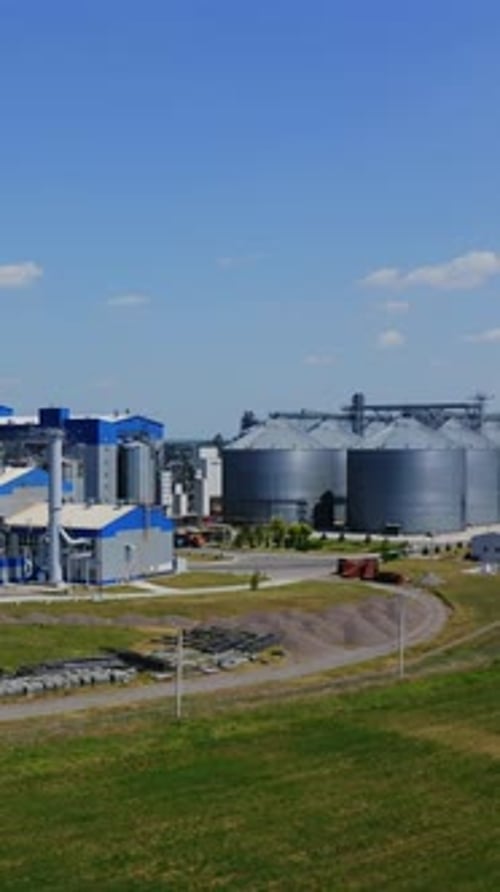Agricultural industry. Modern factory on green field with steel elevators.