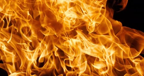 Vibrant close-up of swirling orange fire flames against a dark black backdrop, capturing dynamic