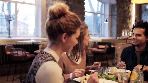 Happy multiethnic friends enjoying food and drinks at restaurant during holidays