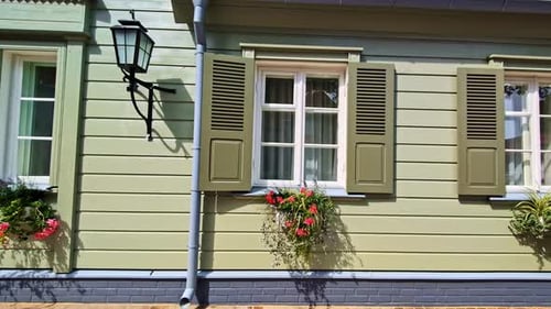 Green wooden house wall with flower boxes and open white window shutters