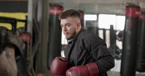 Young Man in Dark Tracksuit and Gloves Doing Boxing Training with Trainer in Gym