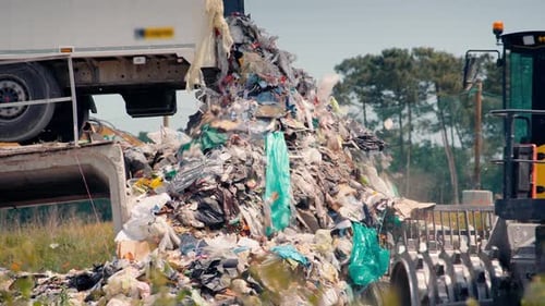 Close-up of a dump truck dumping tons of waste in an open-air landfill.