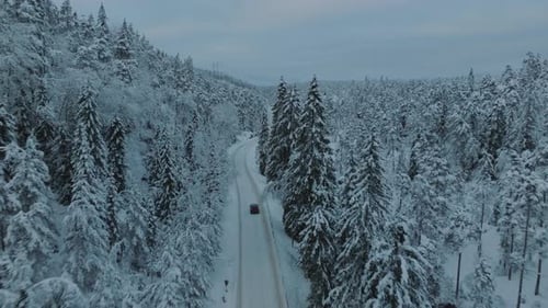 Drone footage of an electric car (EV) driving in beautiful snowy landscape in Norway with snow cover