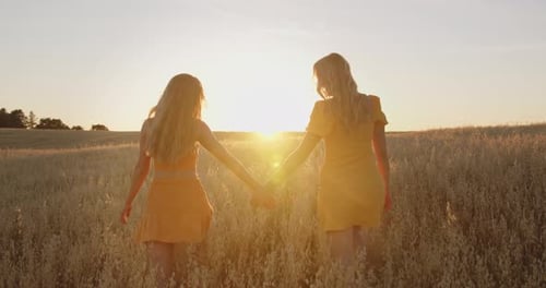 Two Blondes Walk Across the Field Holding Hands