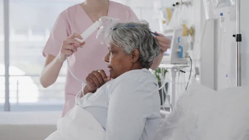 Diverse female doctor giving oxygen mask to senior female patient in hospital bed, slow motion