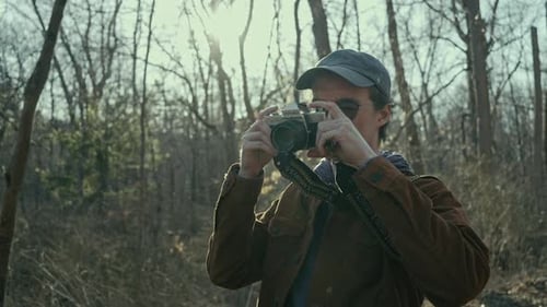 Young Man Photographing in Sunny Forest with Camera