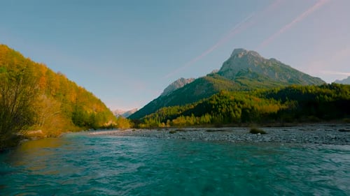 Mountain river, clear blue water rushing by vibrant colorful autumn trees in the sun. Austrian alps