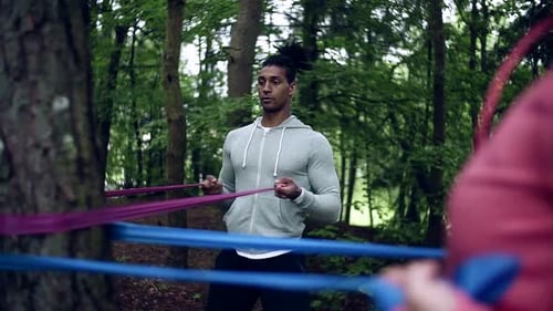 Young couple doing elastic band arm exercises together outdoors in nature