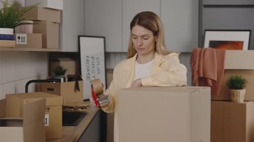 Woman Seals Moving Boxes in a Home