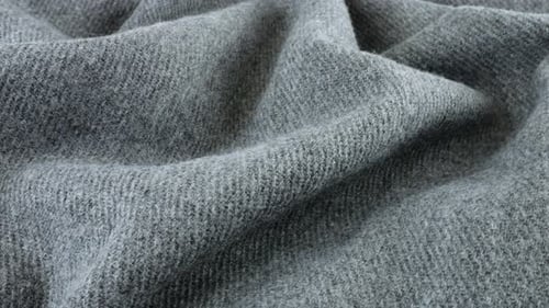 Top view of the soft folds of textured gray wool fabric rotated on the display case.