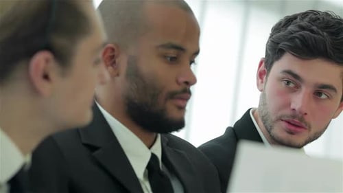 Three Smiling Successful Businessmen Sitting at Table in Office While Discussing