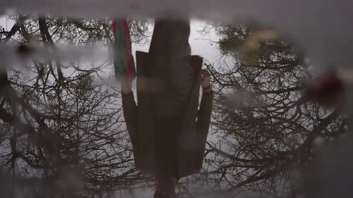 Closeup Puddle on Park Alley with Caucasian Young Man Reflection Passing at Background of Overcast
