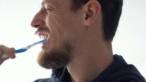 Close up shot of a young man against white background brushing teeth