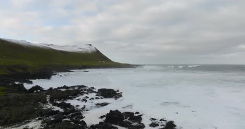 aerial movement over rocky shore of greenland sea at coast of iceland with green grass and mountains