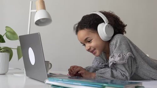 Primary School African American Student Child with Headphones Hand Writing in Book Using Laptop