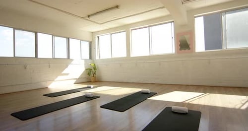 A bright yoga studio features black mats, white walls, and large windows with copy space
