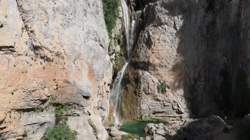 Aerial dolly shot of an exotic waterfall in the mountains, as water curving into stone forming a pon