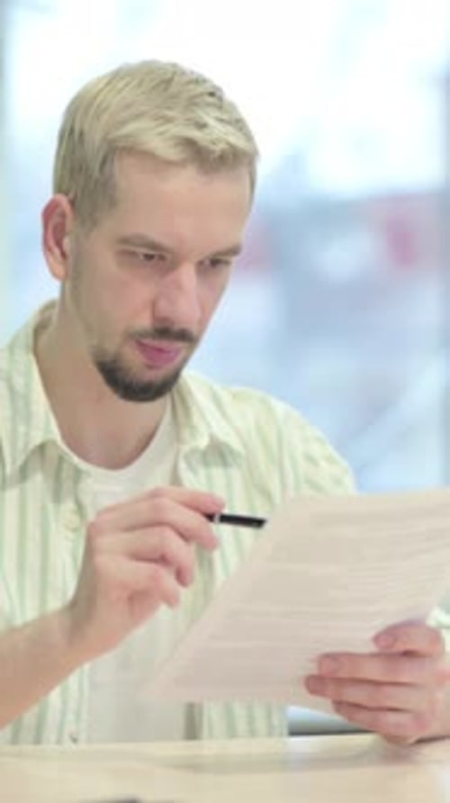 Young Man Reading Documents, Paperwork in Office