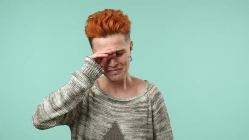 Mujer lesbiana en un suéter abrumada por la emoción y las lágrimas sobre un fondo verde azulado