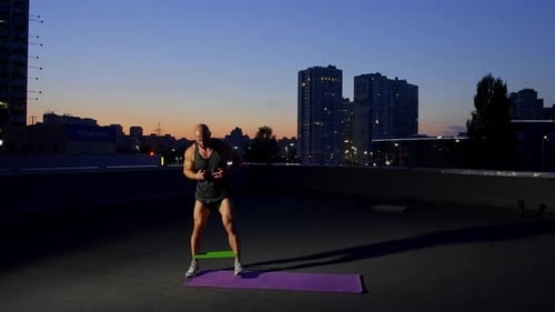 The Athlete Works on the Muscles of the Legs with Help of a Fitness Rubber Band