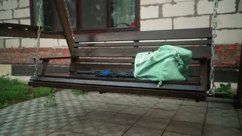 Mint Bag and Blue Umbrella on Outdoor Swing Bench with Greenery and Building Background