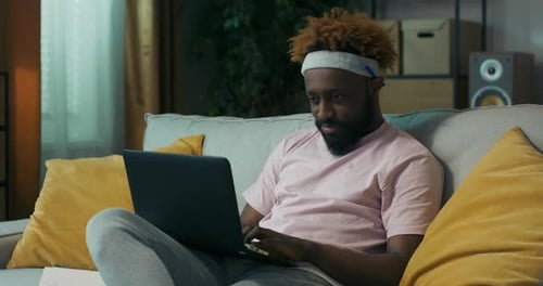 Attractive Man of African Appearance with Beard and Curly Hair Browses Websites on Laptop and Writes
