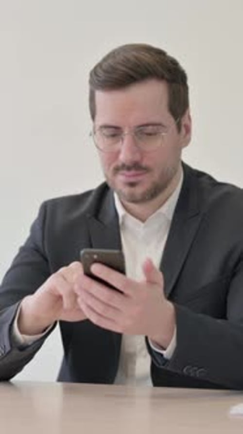 Businessman Browsing Internet on Smartphone in Office, vertical video